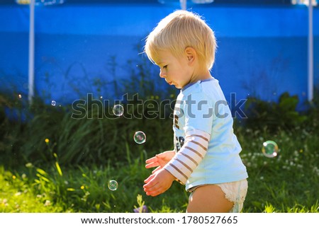 Little blond boy catching soap bubbles in the garden.