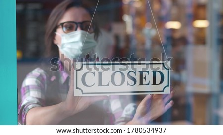 Through glass view of female business owner in safety mask hanging up sign with inscription closed on cafe door. Waitress in protective mask closing restaurant because of pandemic Royalty-Free Stock Photo #1780534937