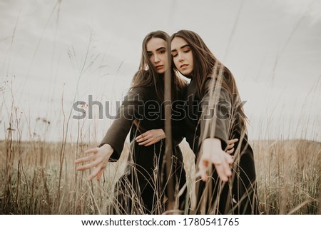 Portrait of beautiful young brunette women sisters with long hair in a coat in a dry yellow grass field. Stylish fashion photography, clothing advertising.