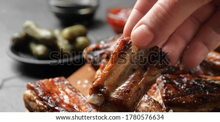 Woman with tasty grilled ribs at table, closeup. Banner design