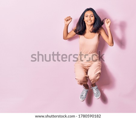 Young beautiful latin woman wearing casual clothes smiling happy. Jumping with smile on face doing winner sign with fists up over isolated pink background