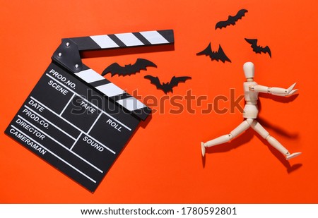 Horror movie, halloween theme. Movie clapperboard, puppet and flying decorative bats on orange bright background. Top view, flat lay