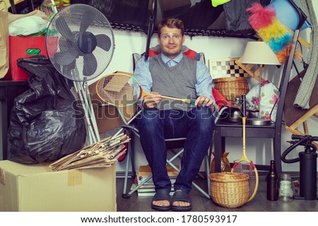 compulsive hoarding disorder concept - man hoarder with stuff piles sitting in the room Royalty-Free Stock Photo #1780593917