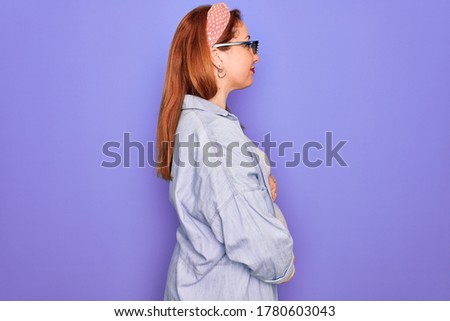 Young redhead pregnant woman expecting baby wearing funny thug life sunglasses looking to side, relax profile pose with natural face with confident smile.
