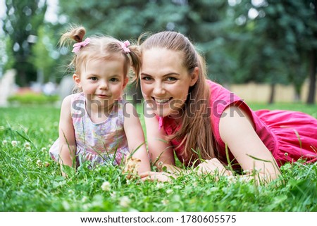 a little girl with her mother is lying on the green grass and looking into the frame