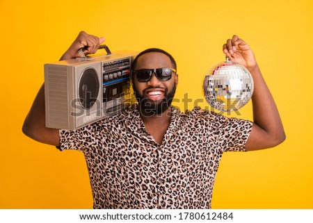 Photo of crazy funny cool dark skin guy hold retro tape recorder glitter disco ball rejoicing summer beach party wear leopard shirt sun glasses isolated yellow background