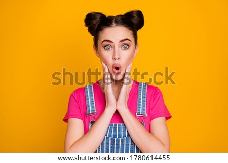 Photo of pretty amazed teen lady good mood open mouth listen cool news arms on cheeks wear casual striped denim overall magenta t-shirt isolated vivid yellow color background