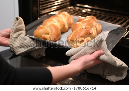 Jewish woman taking out baked Challah Bread from the oven before Sabbath Jewish Holiday. Royalty-Free Stock Photo #1780616714