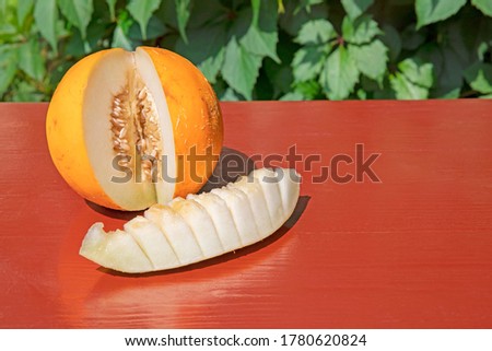 A round melon with a cut-off piece on a mahogany tree. The background is blurry. Free space on the table.