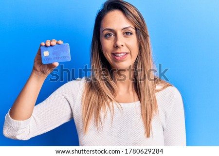 Young beautiful woman holding credit card looking positive and happy standing and smiling with a confident smile showing teeth 