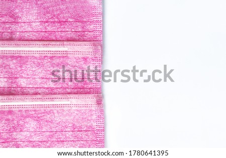 Three pink medical masks lie exactly overlapped on top of each other on a white background to the left