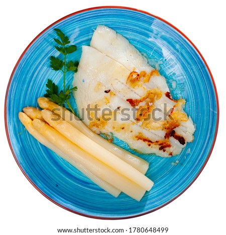 Tasty fried halibut fish fillet with asparagus and greens on plate﻿. Isolated over white background