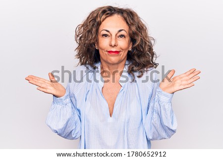 Middle age beautiful brunette woman wearing striped shirt standing over white background clueless and confused with open arms, no idea and doubtful face.