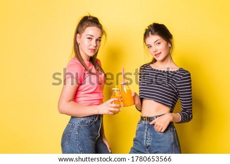 Two cheerful young hipster natural beauty girls posing together on yellow background
