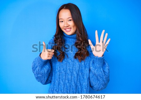 Young beautiful chinese girl wearing casual winter sweater showing and pointing up with fingers number six while smiling confident and happy. 