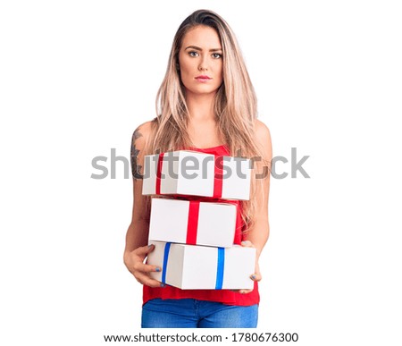 Young beautiful blonde woman holding birthday gifts thinking attitude and sober expression looking self confident 