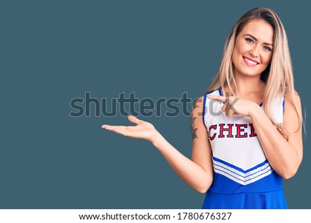 Young beautiful blonde woman wearing cheerleader uniform amazed and smiling to the camera while presenting with hand and pointing with finger. 