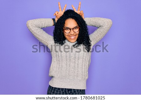 Young african american woman wearing casual sweater and glasses over purple background Posing funny and crazy with fingers on head as bunny ears, smiling cheerful