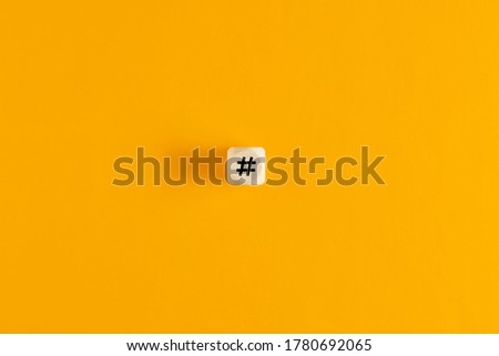Hashtag symbol on wooden cube against yellow background. Minimal overhead view with copy space. 