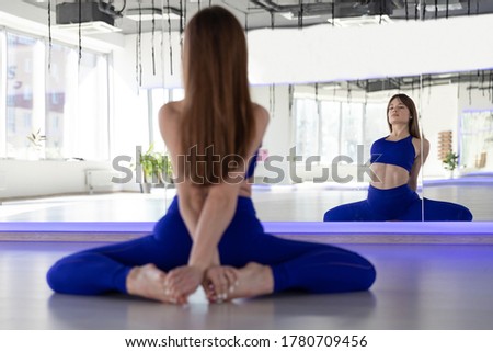 A girl in a blue tracksuit stretches in the yoga room. Training in the morning on a sunny day