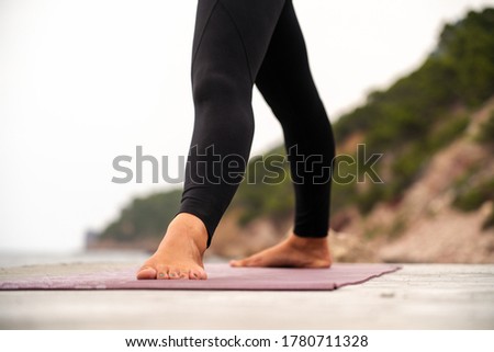 Young brunette woman with curly hair an some dreadlocks doing yoga on a rock at Port of Valldemossa (Mallorca, Spain) minutes before the sunset starts with Serra de Tramuntana at the background