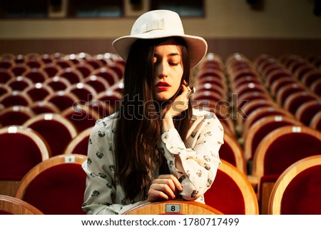 portrait of a pretty girl hipster in a movie theater wearing hat, dreaming alone, fashion lufestyle people concept