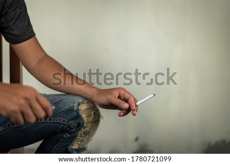man sit on chair and holds a cigarette for smoking   behind the wall. concept for crime, illness, narcotic.