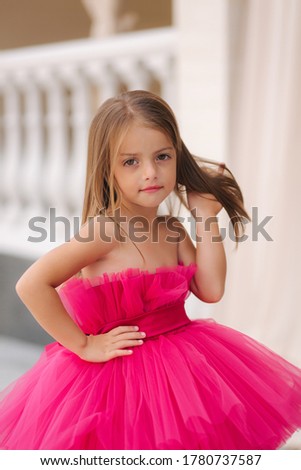 Cute little girl model in fluffy pink dress posing to photographer