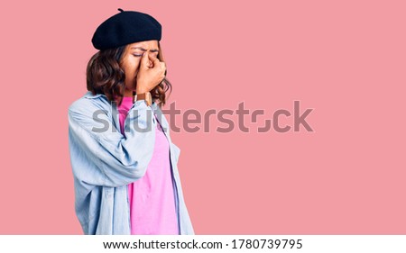 Young beautiful mixed race woman wearing french look with beret tired rubbing nose and eyes feeling fatigue and headache. stress and frustration concept. 