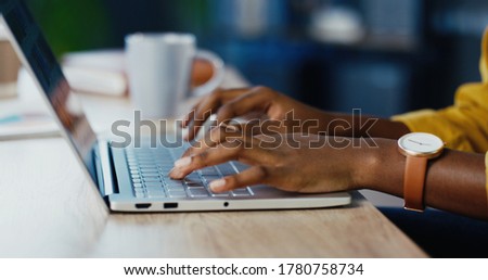 Close up shot of African American female hands typing on laptop while sitting at office desk indoors. Woman fingers tapping and texting on computer keyboard while working in cabinet. Work concept Royalty-Free Stock Photo #1780758734