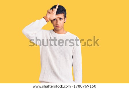 Young african amercian man wearing casual clothes making fun of people with fingers on forehead doing loser gesture mocking and insulting. 