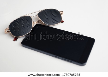 Smartphone and corrective perforated glasses on a white background. Concept, copy space.