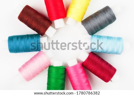 Sewing threads of different colors on reels on a white background in a circle.