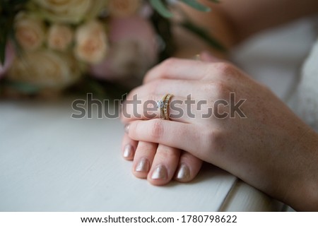 Close up picture of young bride's elegant hands with new beautiful golden engagement diamond ring and wedding ring, shiny nail polish, blurred background