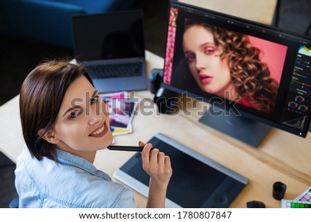 Portrait of graphic designer working in office with laptop,monitor,graphic drawing tablet and color palette.Retouching images in special program.Retoucher workplace in photo studio.Creative agency.