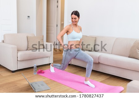 Gorgeous young woman on exercise mat at home and watching workout tutorial online on laptop. Video lesson. Young woman repeating exercises while watching online workout session