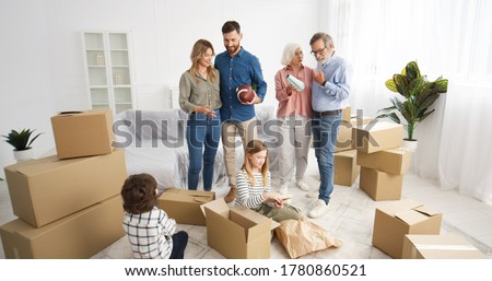 Caucasian parents and grandparents in living room with small cute kids unpacking carton boxes. Family with children and elderly moving in new house after repairment. Replacing in new apartment. Royalty-Free Stock Photo #1780860521