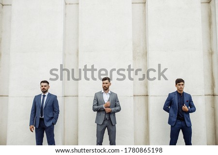 Three men of Caucasian appearance stand at the same distance from each other, wearing luxurious suits. Interesting and creative composition.