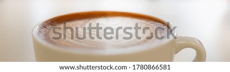 Closeup of white cup of hot coffee latte with milk foam heart shape art. Using for cover page concept.