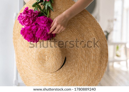 Woman holds in her hand a bouquet of beautiful pink peonies and a straw hat, on a white background. Space for text