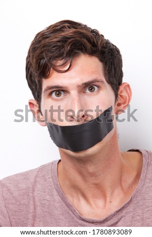 Portrait of young man with tape over his mouth staring over white background