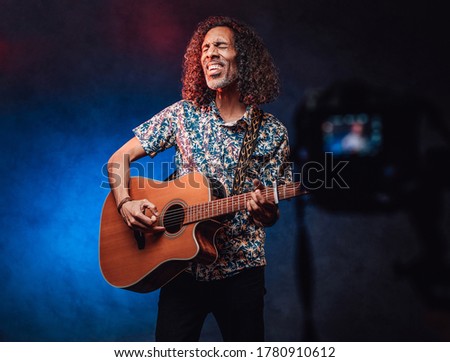 Videographer shoots how a talented Latin American musician playing guitar on a dark background with blue and red light