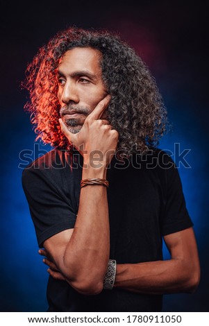 Portrait of a middle aged hispanic male in black t-shirt, lookis pensive. Studio shot on a dark illuminated by blue and red light