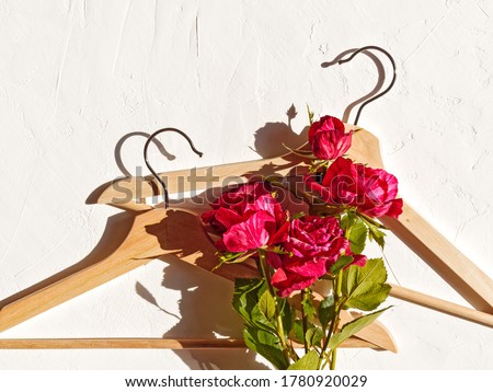 Fashionable flower arrangement. Layout of red rose flowers and wooden coat hanger. Template for sales of clothing, accessories, underwear. Flat lay. Top view. Copy space. Royalty-Free Stock Photo #1780920029