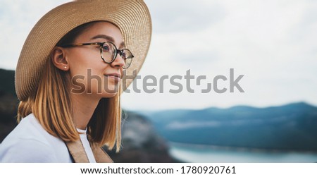 portrait of relaxing young girl tourist with light hair in straw summer hat and hipster glasses background of blue sky and natural mountain landscape, empty space for your design