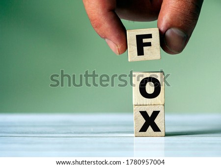 The hand puts the cube block with the inscription FOX