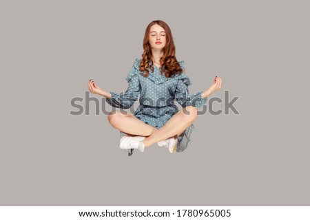 Hovering in air. Calm peaceful relaxed girl ruffle dress levitating with mudra gesture hands up, closed eyes, meditating sitting in yoga position. indoor studio shot isolated on gray background Royalty-Free Stock Photo #1780965005