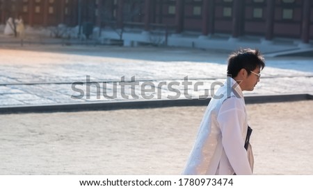 Korean man in traditional dress, Hanbok at Korean traditional palace. Asian male in Korean dress called Hanbok standing and looking at people outdoor near wall of temple or palace with copy space.
