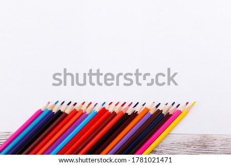 Colored pencils on paper on wooden table, art concept. White A4 paper sheets with many pencils on desktop. Mockup template. Drawing a still life