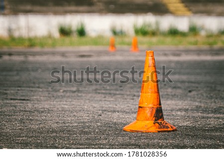 Close-up of an old dirty orange traffic cone at the site for driving training or auto school. Plastic red markings at the autodrome, extreme driving stadium. Driving school concept.